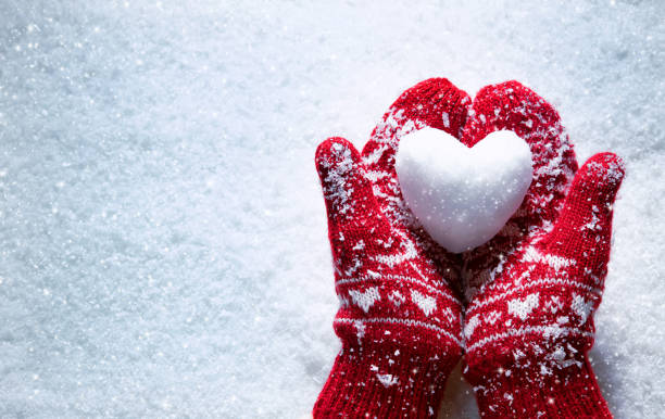 Female+hands+in+knitted+mittens+with+snowy+heart+against+snow+background.+Love%2C+winter+and+Valentines+day+romantic+creative+concept+with+copy+space+for+text